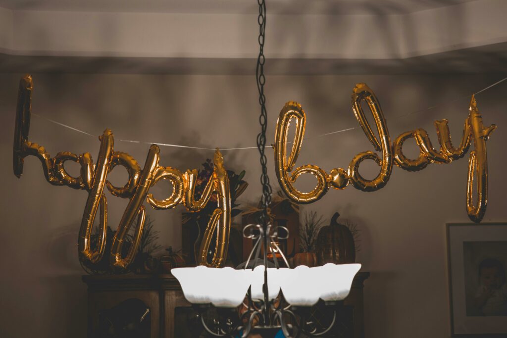 Festive gold balloons spelling 'happy bday' hang indoors, ideal for party themes.
